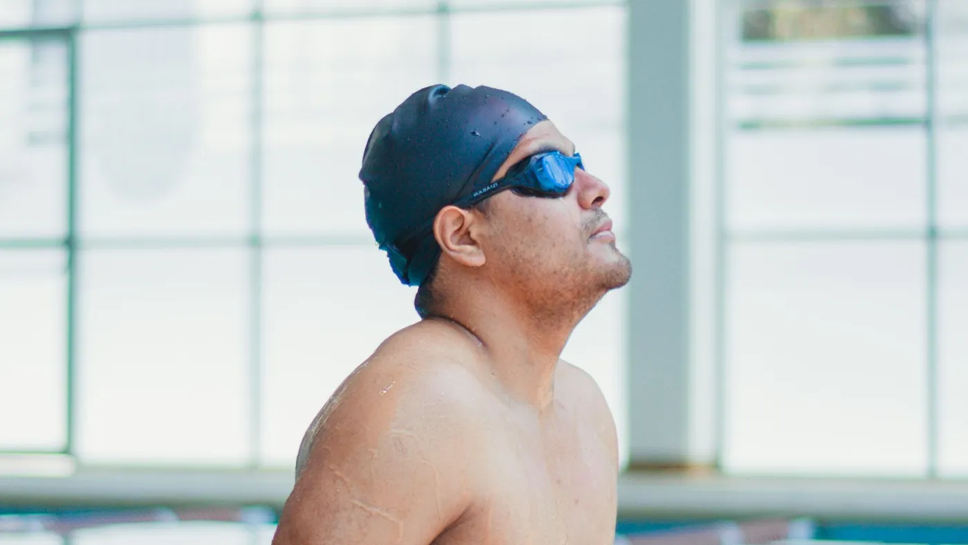 Schwimmer mit Badekappe und Brille blickt am Beckenrand nach oben