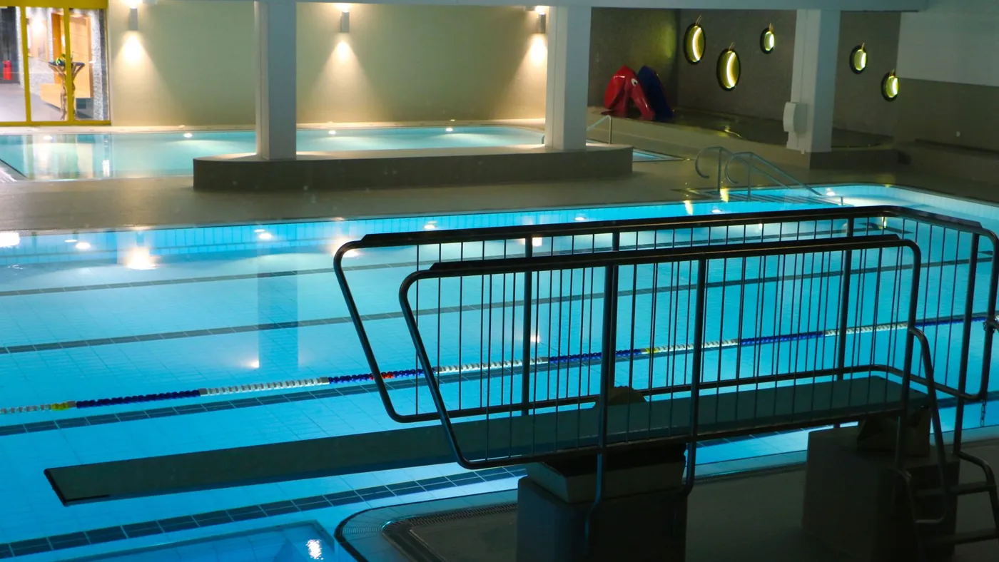 Hallenbad am Abend mit beleuchtetem Becken und Treppengeländer
