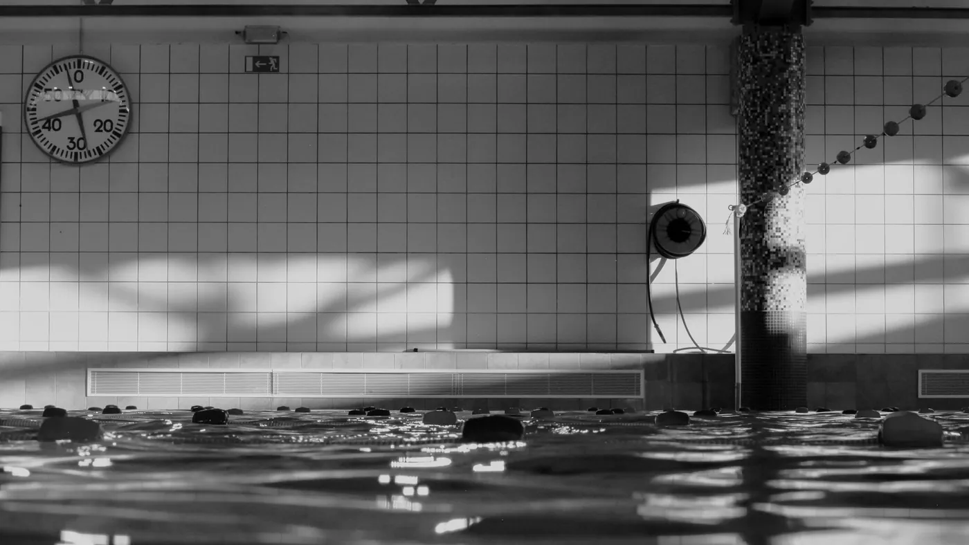 Hallenbad in Schwarzweiss, Uhr an der gekachelten Wand und Spiegelung auf dem Wasser