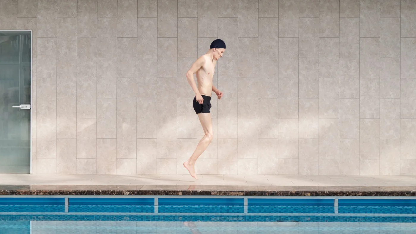 Person springt vom Beckenrand ins Wasser eines hellen Hallenbads